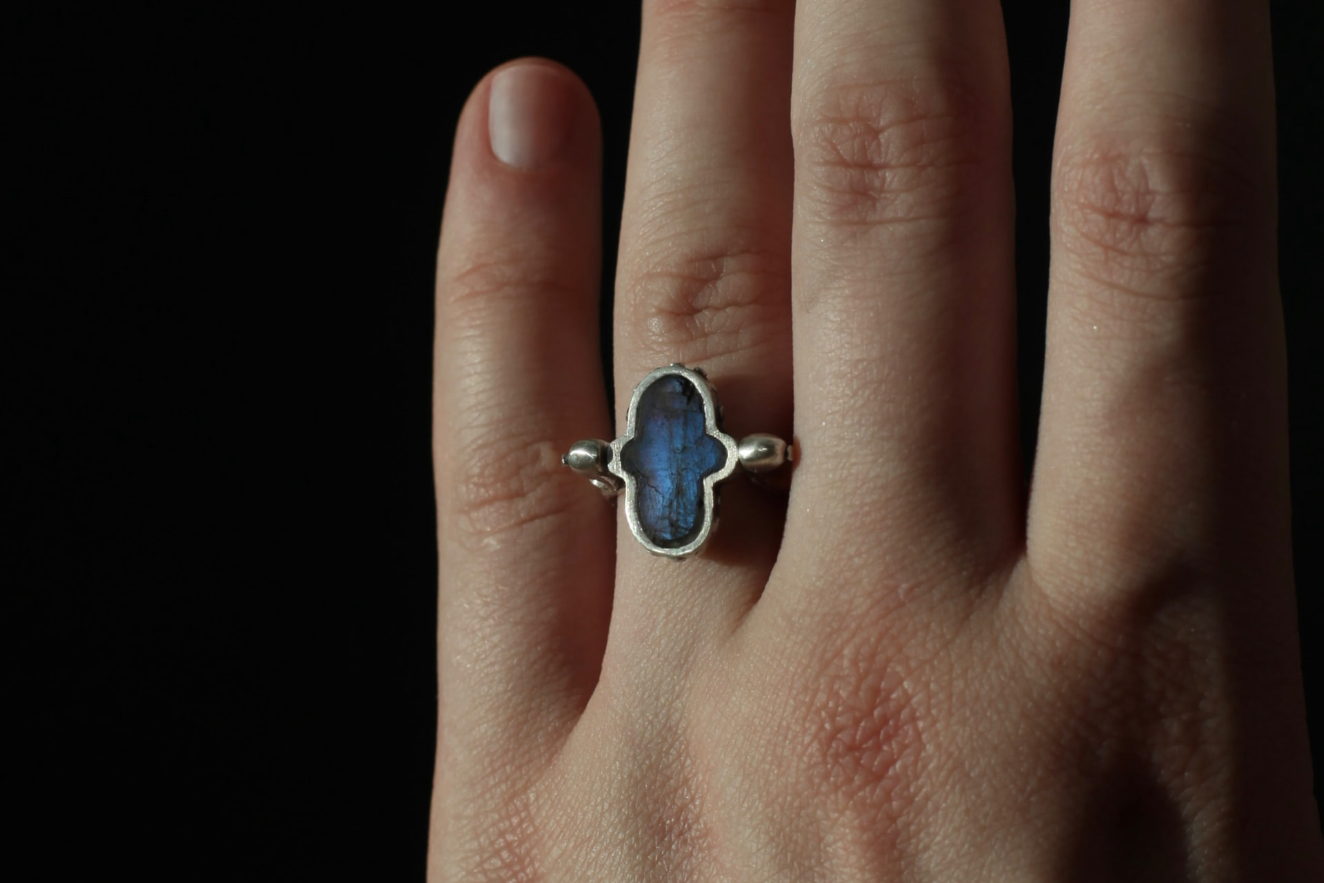 Silver ring with a deep blue labradorite stone worn on the hand against a dark background