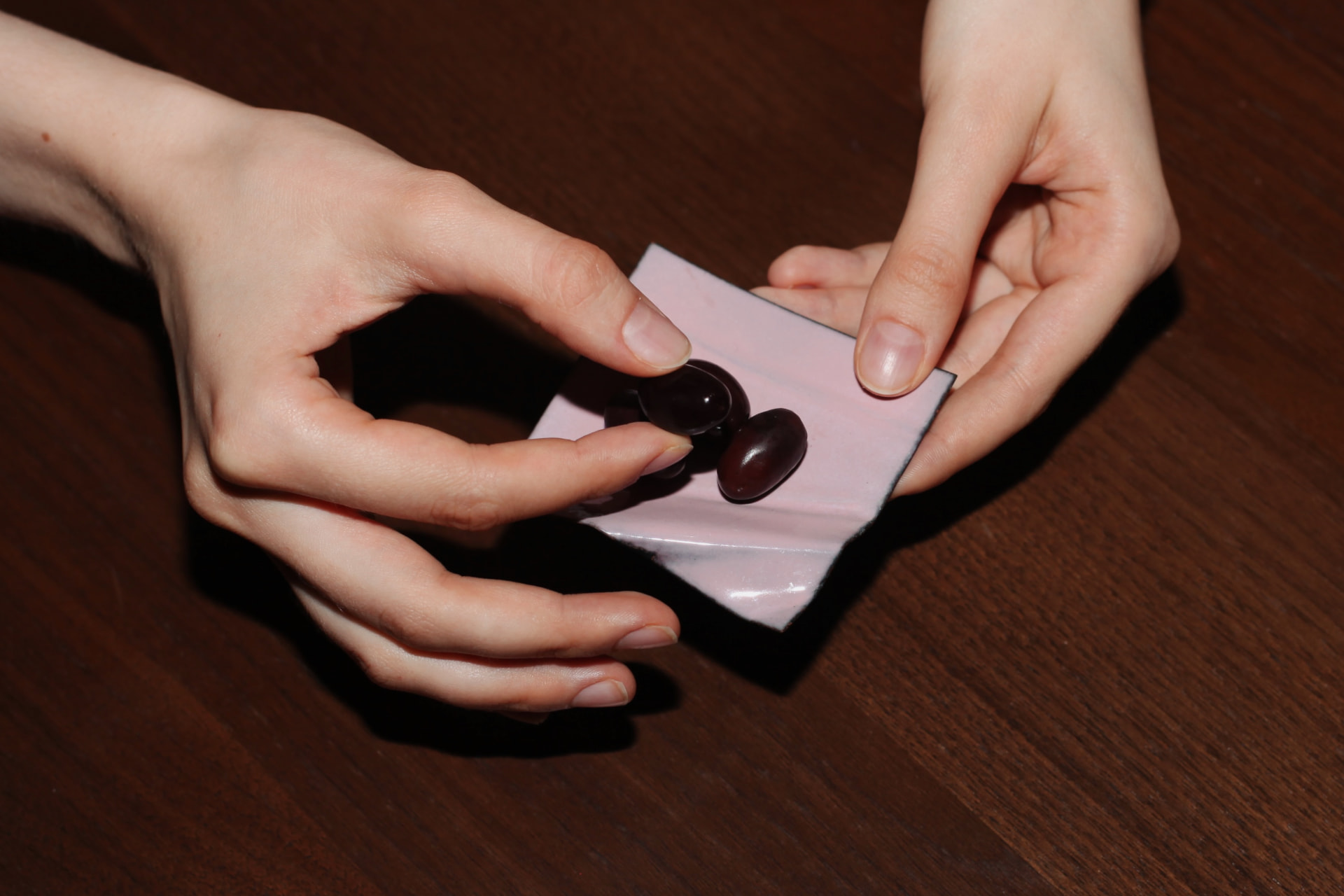 Two hands holding a small pink enameled copper square with dark olives